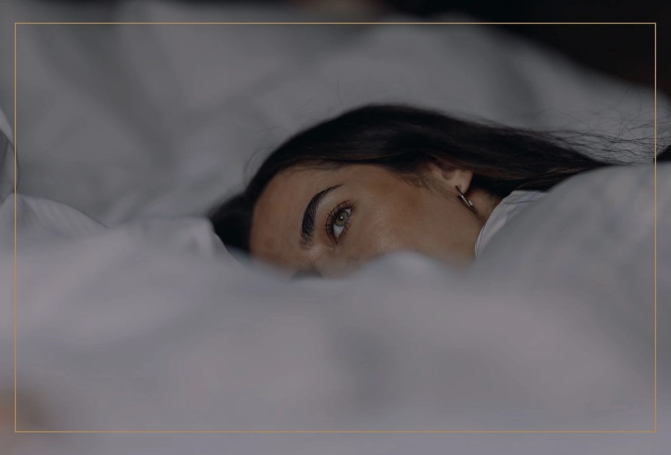 Kvinna i pyjamas vilar i en skön och krispigt vit hotellsäng på Vimmerby Stadshotell och blickar ut genom fönstret. En stund av lugn och komfort – klicka för att läsa mer om vad som alltid ingår hos oss.