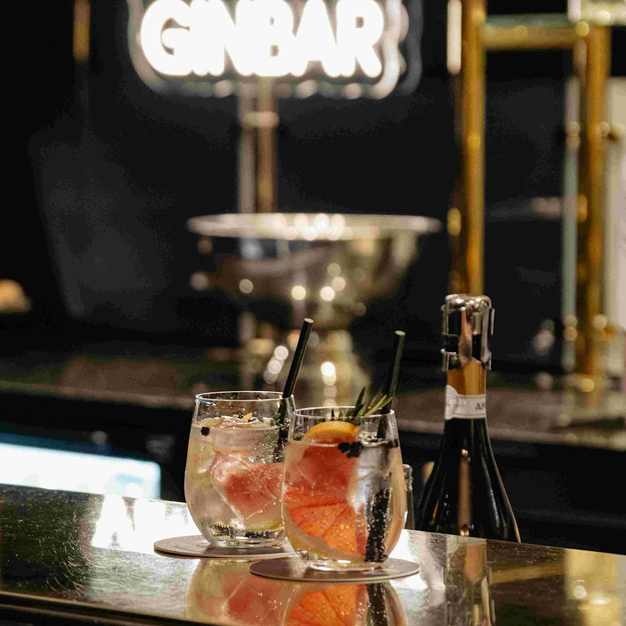Två läskande gin & tonic på baren på Vimmerby Stadshotell – Vimmerby Spritfabriks signatur-GT med blodapelsin och kvist. I bakgrunden syns neonskylten för Vimmerby Ginbar.