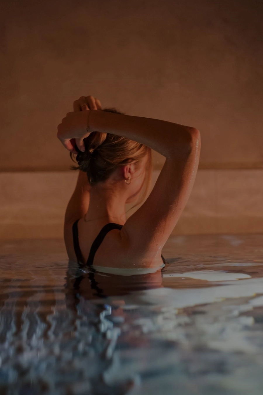 Kvinna i en stilla, varm pool på Vimmerby Stadshotell Spa. Hon håller upp håret i det mjuka källarvalvets sken – en stund av lugn och återhämtning. Klicka för att läsa mer om vårt spa.