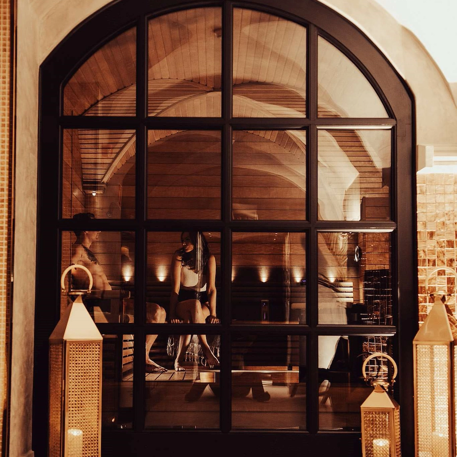 Inblick i torrbastun på Vimmerby Stadshotell Spa – valvformat fönster med svarta spröjs och stora pampiga ljuslyktor. En man och en kvinna sitter i bastun och njuter av en lugn stund tillsammans.