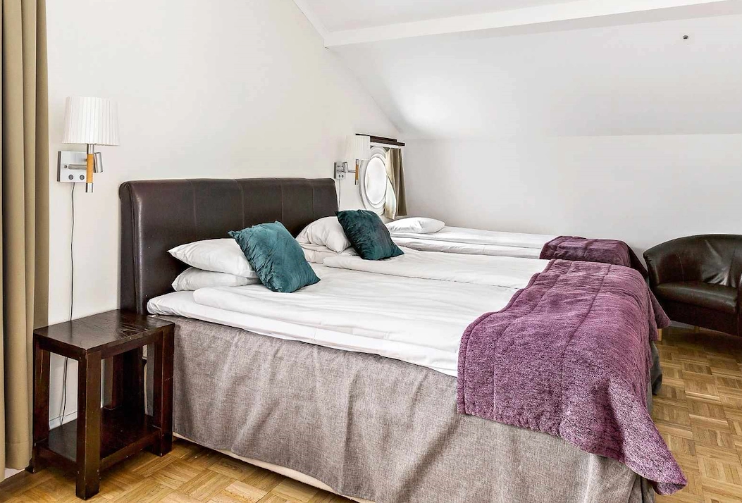 Familjerum på Vimmerby Stadshotell med dubbelsäng och enkelsäng i ett ljust rum med mörka trädetaljer. Bekvämt och praktiskt för en familj som reser tillsammans.