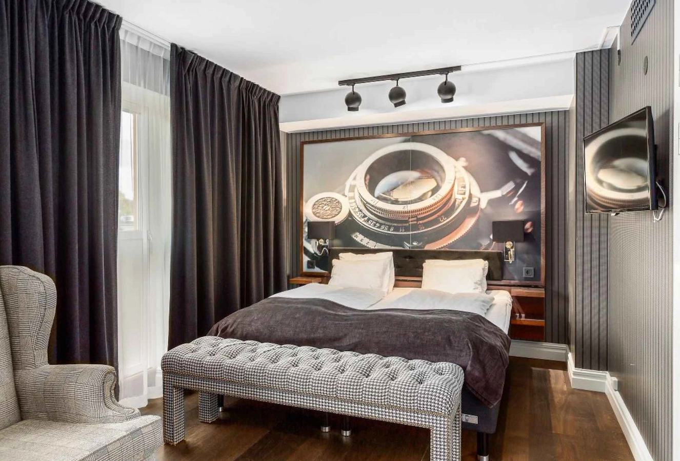 Unikt familjerum classic på Vimmerby Stadshotell – inrett i mörkare stil med många fina detaljer. Skön Carpe Diem-säng, rutmönstrad bänk, fåtölj och balkongdörr som släpper in ljuset.