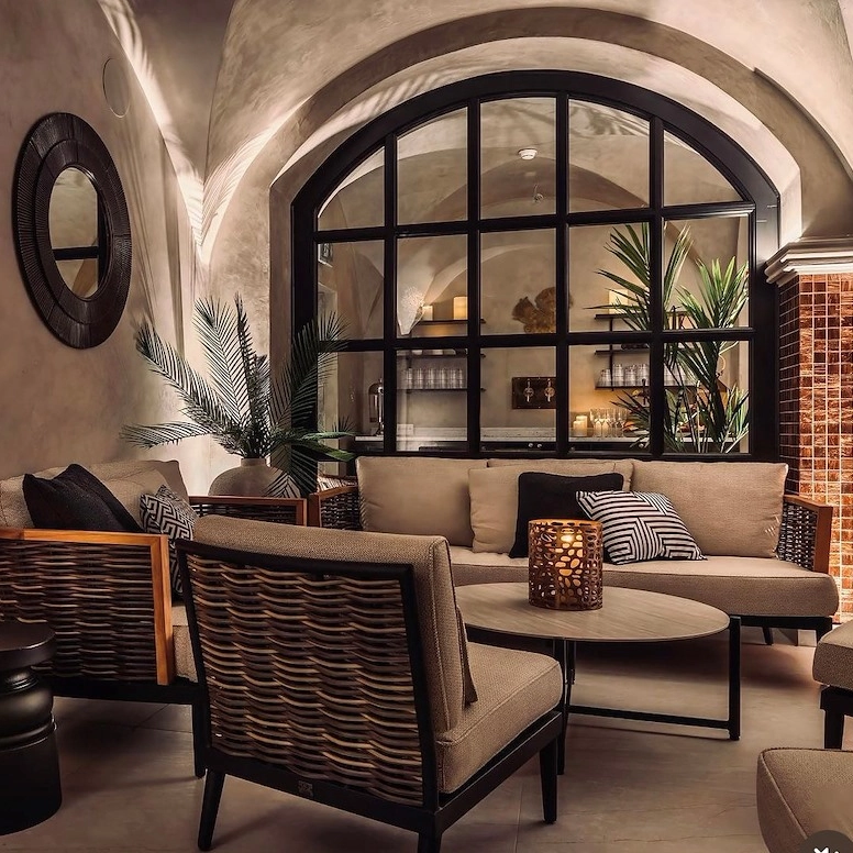 Noggrant inredd loungehörna på Vimmerby Stadshotell Spa – soffa, fåtöljer, ljuslyktor och valv i varm, prisbelönt design med palmblad som accent.