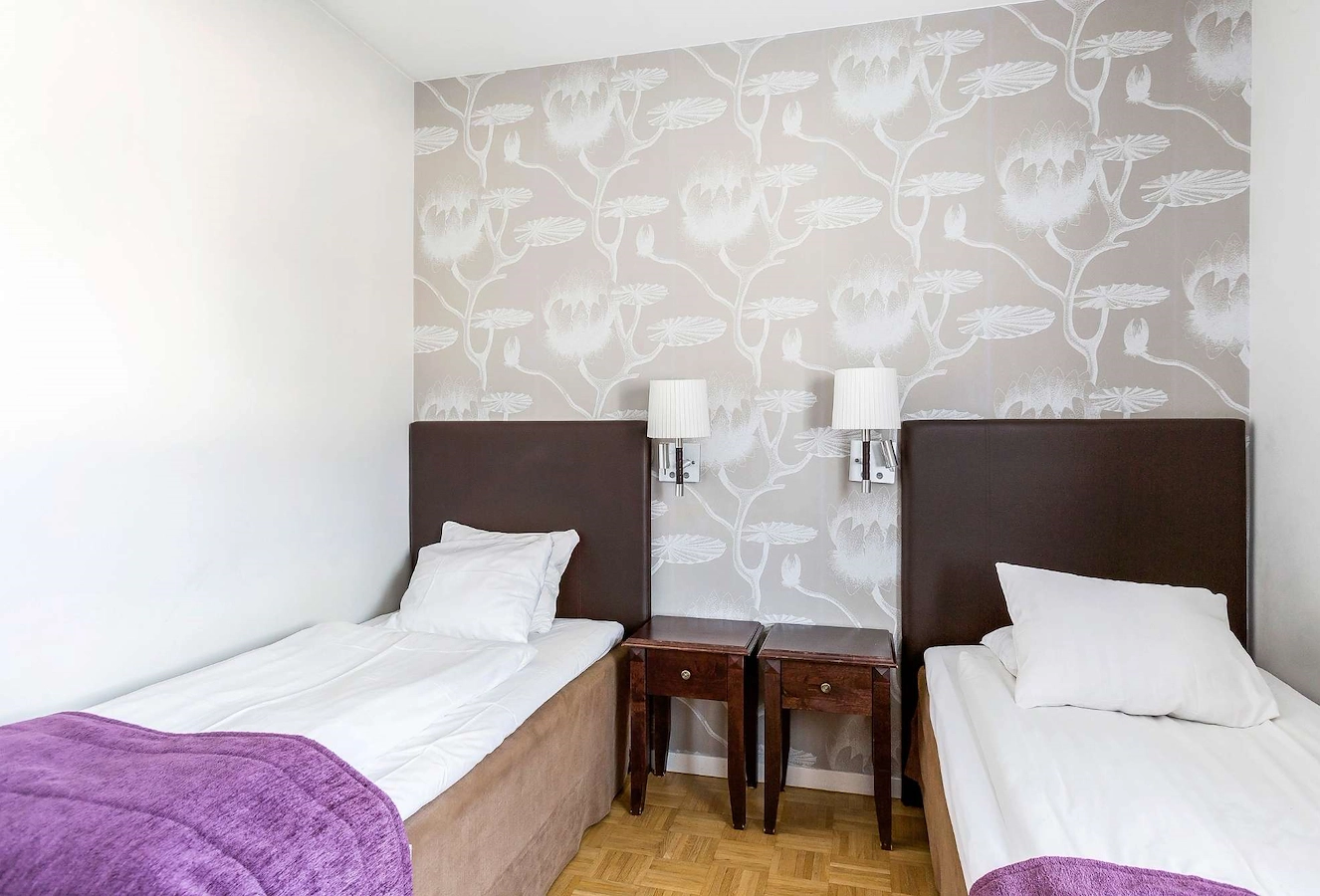 Twin-rum på Vimmerby Stadshotell med två separata 90 cm-sängar, ljusa väggar, beige fondvägg och krispigt vita lakan. Mörka trädetaljer i brunt ger en varm och klassisk känsla.